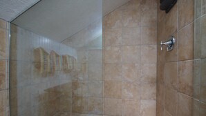 Une salle de bain avec des carreaux de couleur beige, une douche en verre et un robinet fixé au mur.