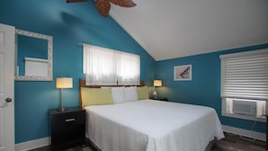 Une chambre à coucher comprenant un lit, deux tables de chevet avec des lampes, une fenêtre avec des stores, un ventilateur de plafond et un climatiseur fixé au mur.