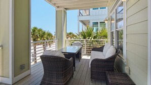 Un patio techado al aire libre con mobiliario de mimbre y una mesa, con vistas a un edificio con balcón.