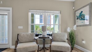 Una habitación con dos sillones tapizados frente a una mesa con una lámpara, una ventana con vistas a edificios y una obra de arte enmarcada en la pared.