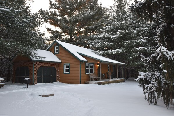 A wooden cabin with a snow-covered roof, surrounded by evergreen trees.