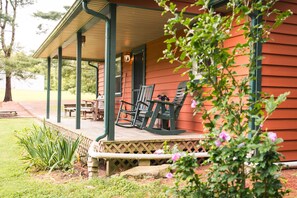 A porch with wooden chairs and a table, surrounded by a garden with plants and flowers.