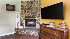 A stone fireplace with a TV mounted on the wall above it, a wooden dresser with drawers, and a sign that reads "Welcome to Cottage." - Woodland view-Cedar Cottage (Laurelville)