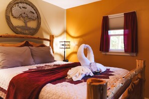 A neatly made bed with a red blanket, a wooden headboard, and a wall-mounted tree artwork.