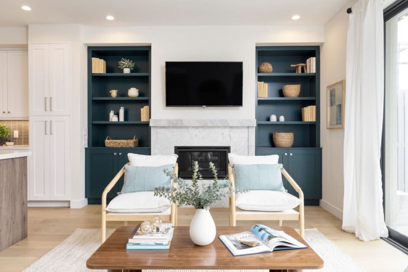 A living room with two armchairs, a coffee table, a fireplace, and built-in shelving with books and decorative items.