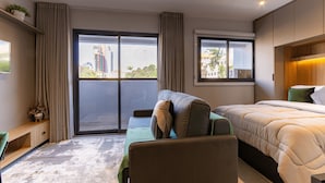A modern hotel room with a large bed, a sofa, a small table, and a view of the city through the windows. - Essence Studio Vila Mariana | Air Conditioning, Wi-Fi & Vila Mariana Metro (São Paulo)