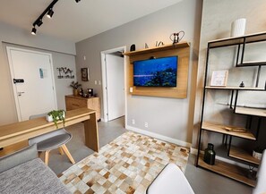 Un salon moderne avec un bureau en bois, un téléviseur fixé au mur, un tapis à motifs et une bibliothèque.