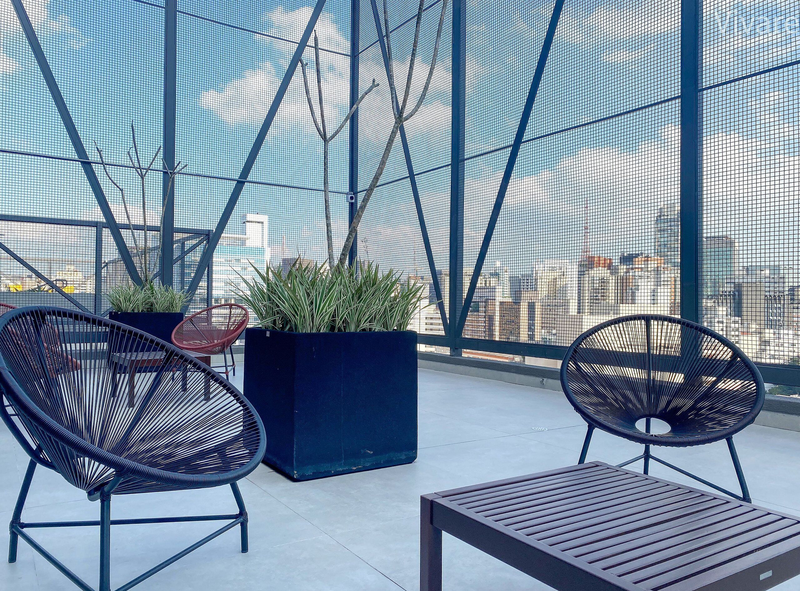 Une terrasse sur le toit, avec deux chaises noires en osier, une table en bois et un jardinier contenant des plantes vertes.