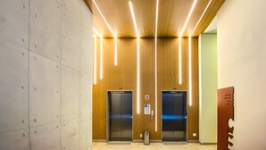 Een interieur met twee liften, houten lambrisering en een metalen prullenbak.