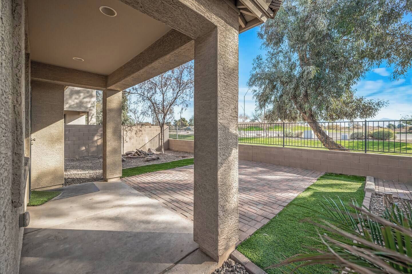 Un patio couvert doté d’un sol en béton, d’un mur en briques et offrant une vue sur un jardin aménagé avec des arbres et une clôture.