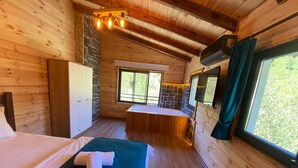 A wooden cabin room with a bed, a small bathroom, and a window with a view of greenery. - Nika Otel (Camlihemsin)