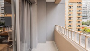 Un balcón con puerta de cristal, una pequeña mesa con sillas y vista a un edificio alto con balcones.