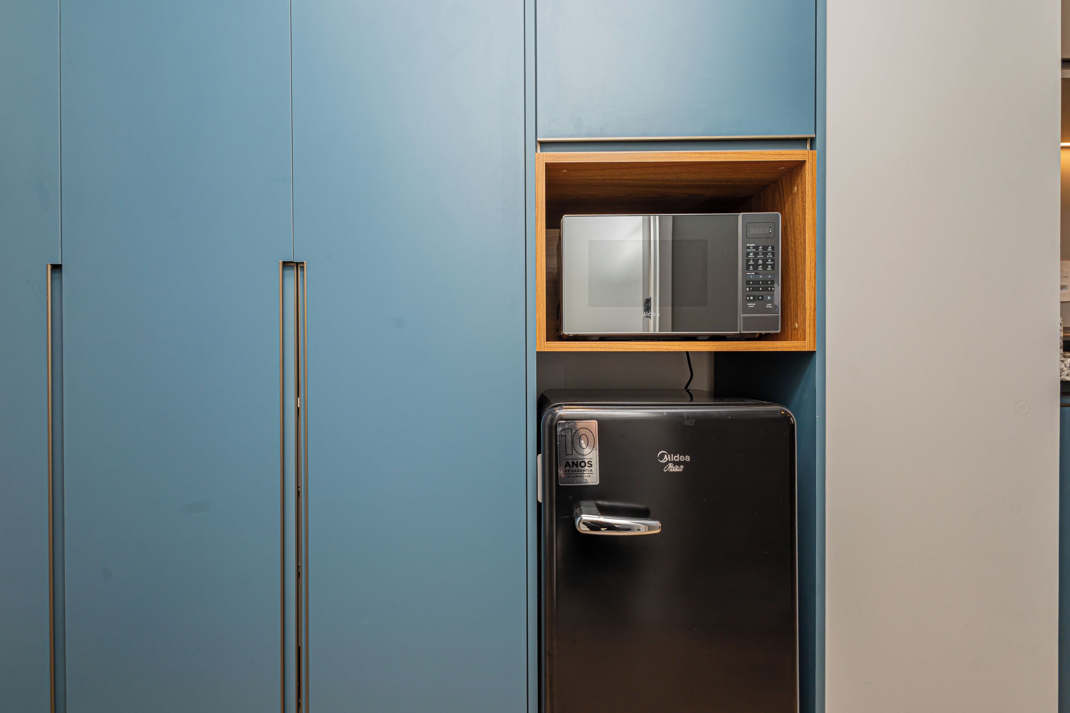 Cocina compacta con un microondas en un estante sobre un refrigerador.
