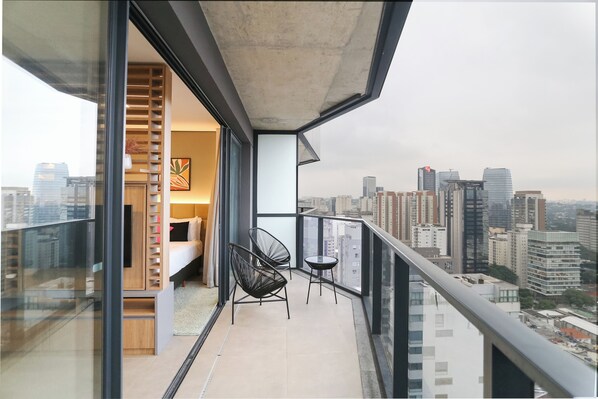 A balcony with a city view, a bed, and two chairs. - VN Millenium Faria Lima (Sao Paulo)