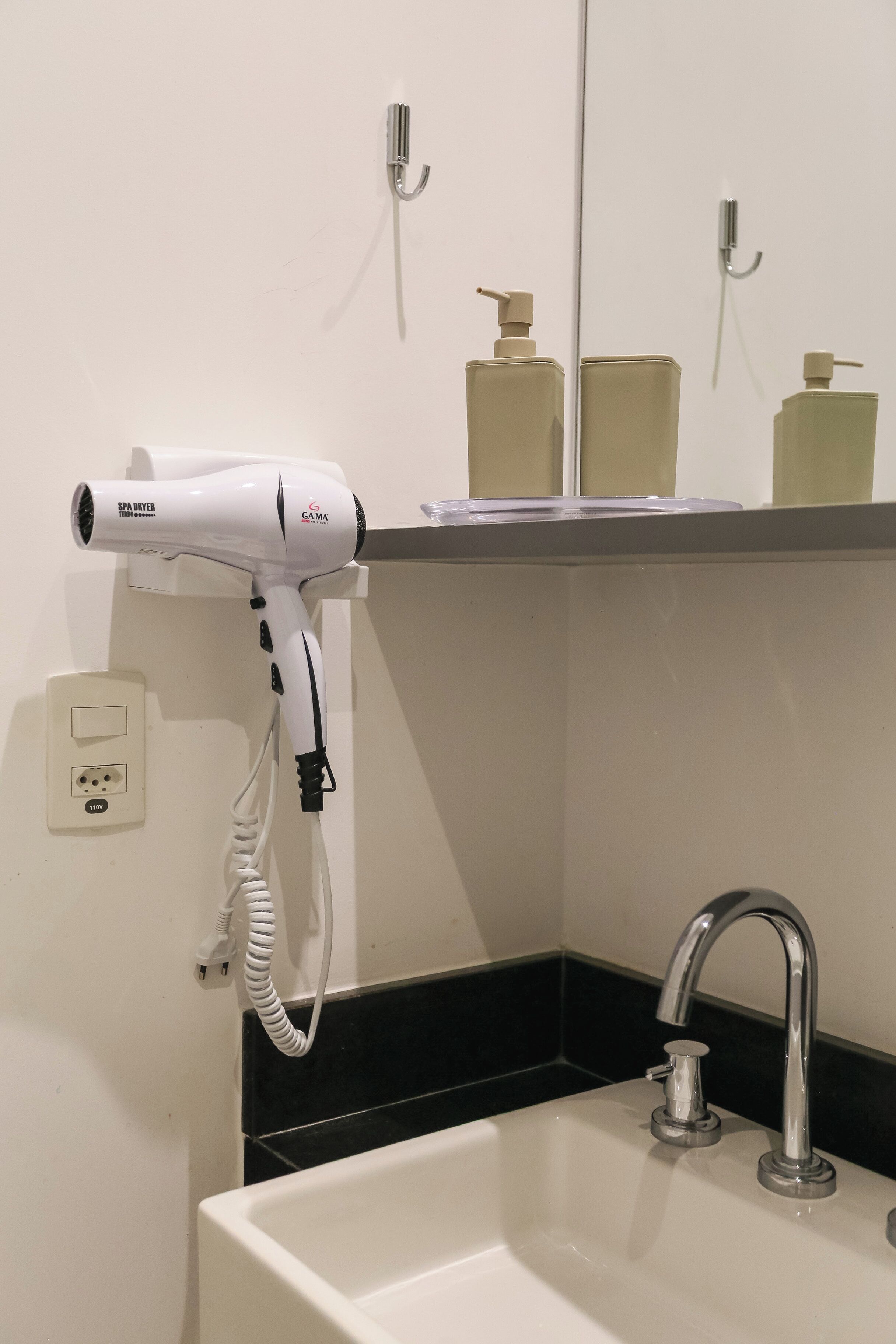 Un baño con un lavabo blanco, un espejo, un secador de pelo y una repisa con artículos de aseo.