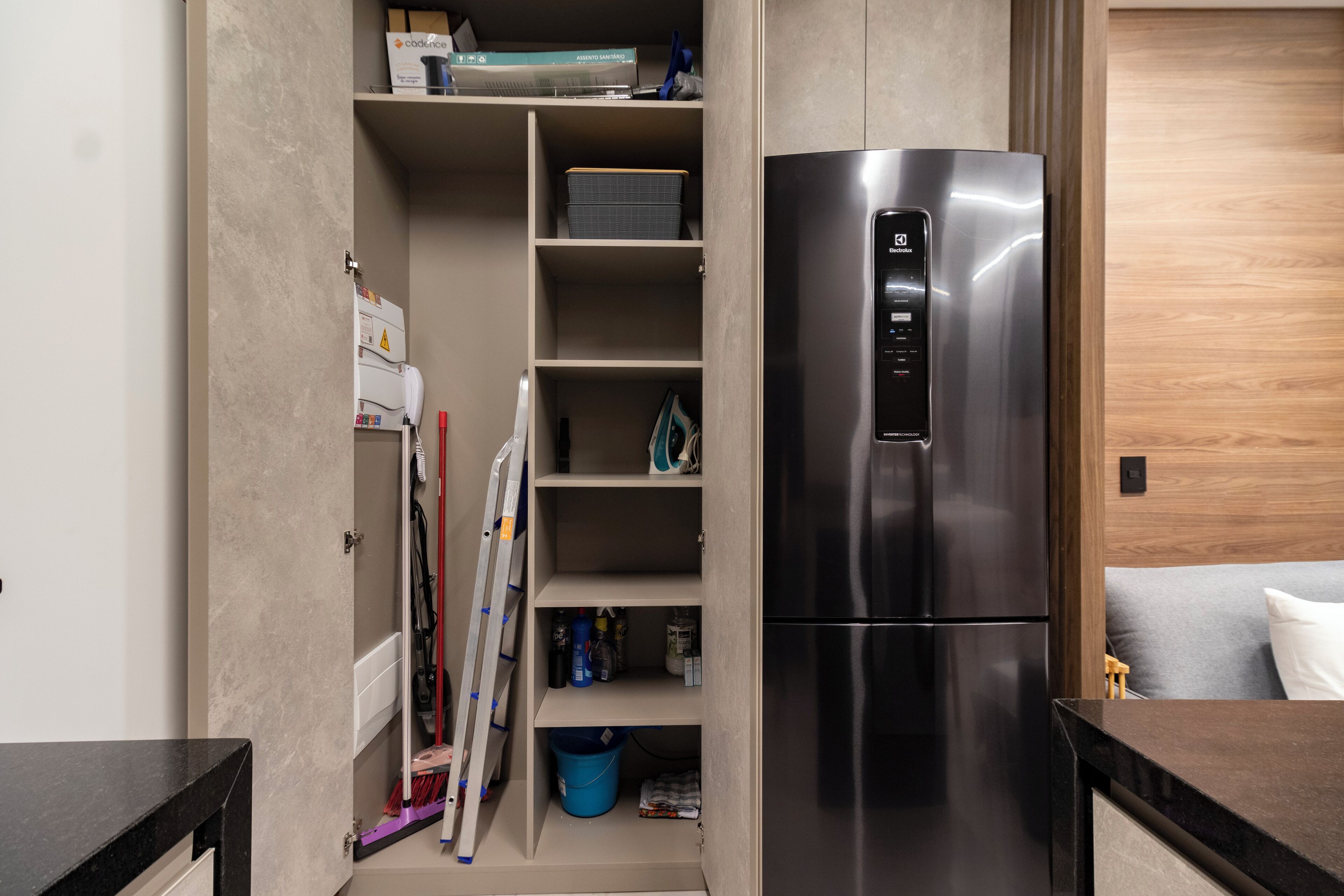 A compact kitchen with a built-in stainless steel refrigerator, a wooden cabinet with shelves, and a small seating area with a cushion.