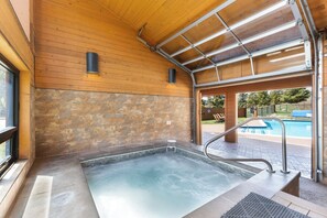 A spa area with a hot tub, wooden walls, stone accents, and a view of an outdoor pool. - Tt1321-2 (Keystone)