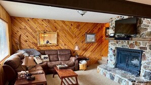 Un salon chaleureux avec une cheminée en pierre, des murs en bois, un canapé en cuir et un téléviseur.