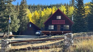 Une cabane avec un toit rouge et un petit porche, entourée d’arbres et sous un ciel dégagé.