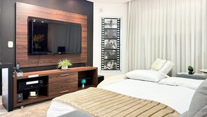 Un dormitorio moderno con una cama grande, un televisor montado en la pared, una mesita de noche y una ventana con cortinas.