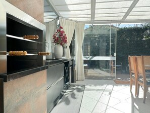 A modern kitchen with a built-in oven and wooden handles, a large window with curtains, and a patio area with a table and chairs. - Casa Moderna e Aconchegante  (Florianopolis)