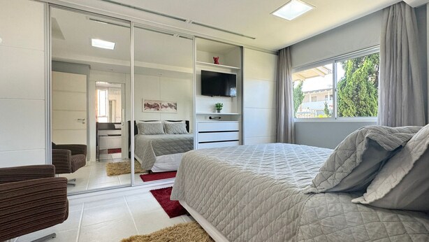 A modern bedroom with a large bed, a TV, a sliding closet, and a view of the outdoors. - Casa Moderna e Aconchegante  (Florianopolis)