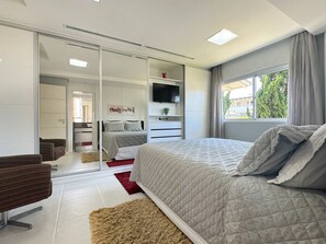 A modern bedroom with a large bed, a TV, a sliding closet, and a view of the outdoors. - Casa Moderna e Aconchegante  (Florianopolis)
