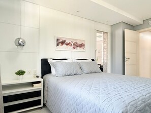 A bedroom with a bed, a bedside table, a wall-mounted light, and a door. - Casa Moderna e Aconchegante  (Florianopolis)
