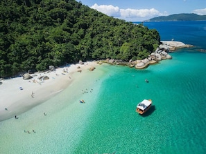 An aerial view of a beach with clear turquoise waters, a sandy shore, and a forested hillside. - Casa Moderna e Aconchegante  (Florianopolis)