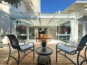 An outdoor patio with two wicker chairs and a small table, a glass-enclosed dining area, and a view of the interior. - Casa Moderna e Aconchegante  (Florianopolis)