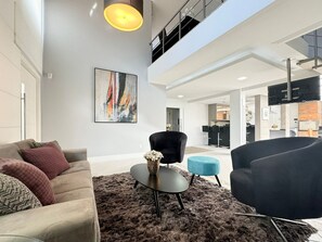 A modern living room with a high ceiling, a large abstract painting, and a view of the kitchen and dining area. - Casa Moderna e Aconchegante  (Florianopolis)