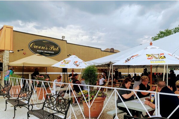 Un espacio al aire libre con mesas y sillas, sombrillas y un edificio con un cartel que dice "Owen's Pub North Wildwood".