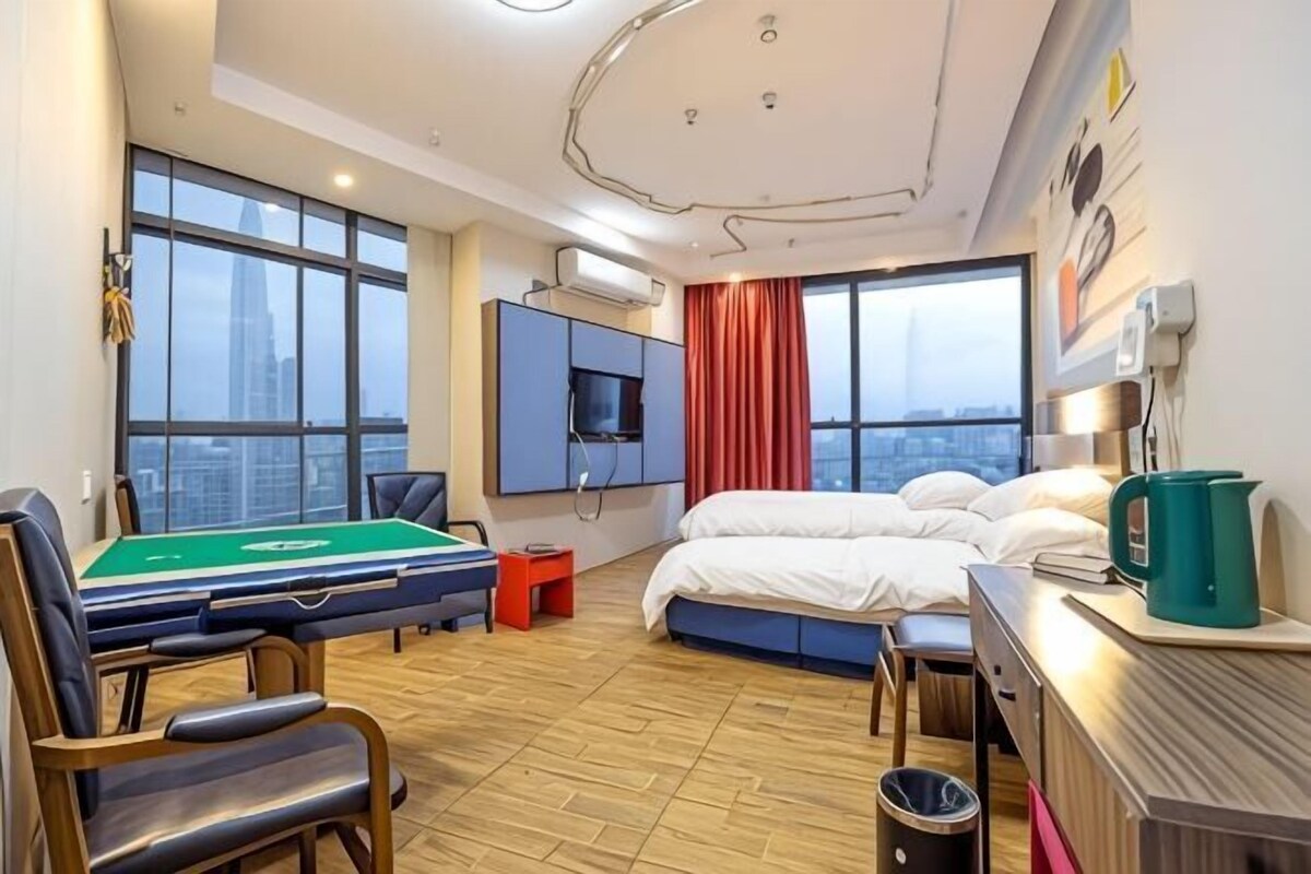 A hotel room with a pool table, a bed, a desk, and a view of the city.