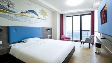 A hotel room with a large bed, a desk, a chair, a TV, and a window with curtains.
