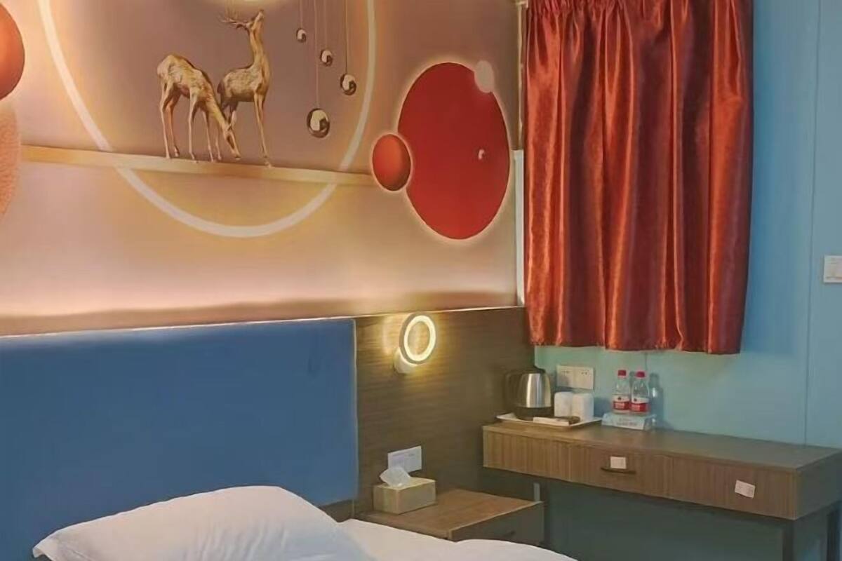Une chambre d’hôtel avec un lit, une table de chevet avec une lampe, un miroir et un mur orné d’œuvres d’art abstraites.