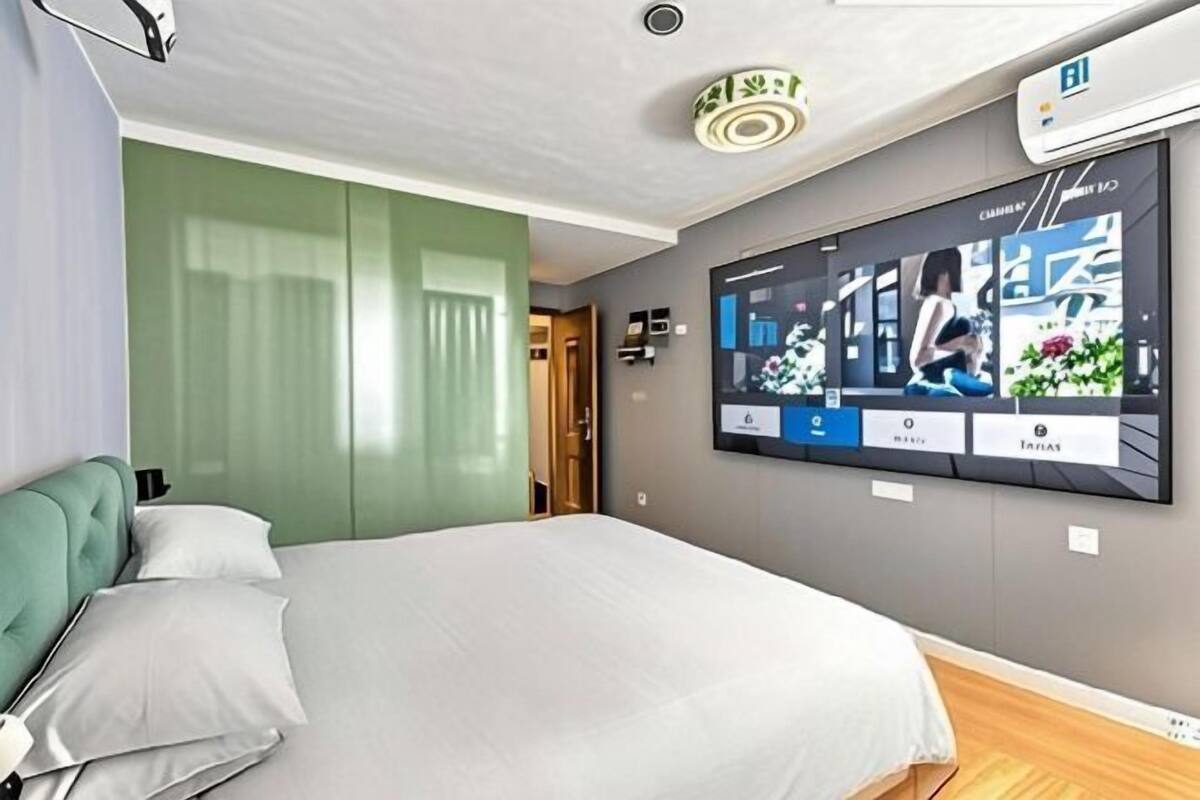 Une chambre d’hôtel moderne dotée d’un grand lit, d’un téléviseur à écran plat fixé au mur et d’un mur d’accent de couleur verte.
