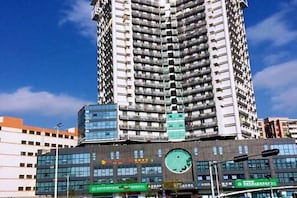 Um edifício alto com vários andares, um relógio na fachada e sinalização indicando uma área comercial.