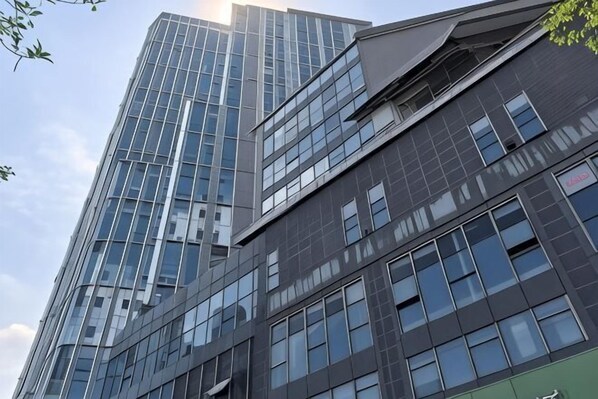 Un bâtiment moderne à plusieurs étages, doté de grandes fenêtres et d’une façade combinant des éléments en verre et des matériaux foncés.