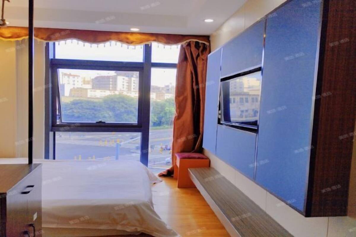 Une chambre d’hôtel avec un lit, un téléviseur fixé au mur, une fenêtre donnant sur des immeubles et un banc près de la fenêtre.
