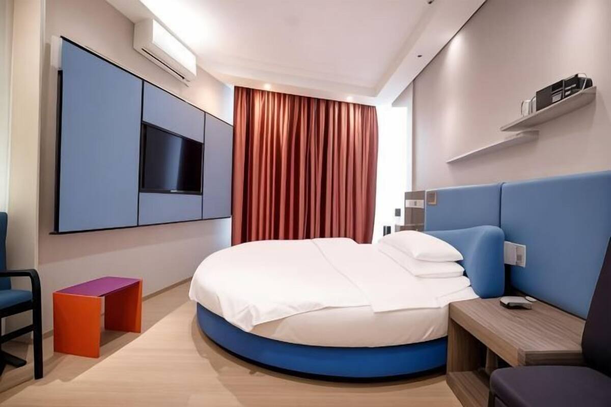 Une chambre d’hôtel moderne avec un lit rond, un téléviseur fixé au mur et une petite table.