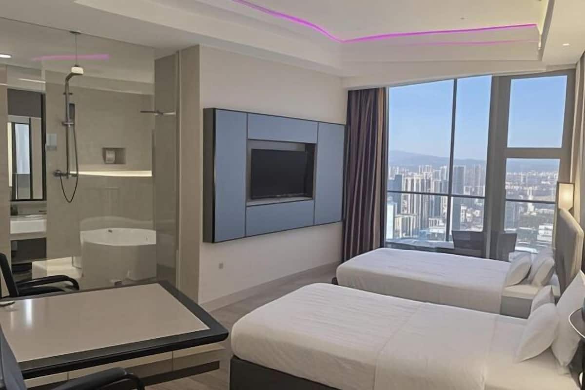 Une chambre d’hôtel moderne dotée d’une grande fenêtre donnant sur la ville, d’un téléviseur à écran plat fixé au mur et d’un espace salle de bain séparé.