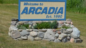 A welcome sign for ARCADIA established in 1880, surrounded by a stone wall and greenery. - Pet-Friendly Family Home near Golf, LK MI, M22 (Arcadia)
