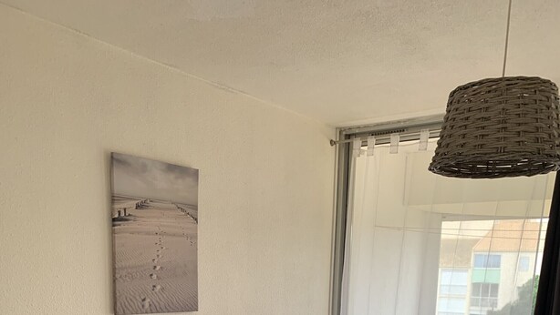 A bedroom with a bed, a window with a view of buildings, a picture on the wall, and a hanging light fixture. - Solydays Floralies duplex for 6 people near the beach (Le Grau-du-Roi)