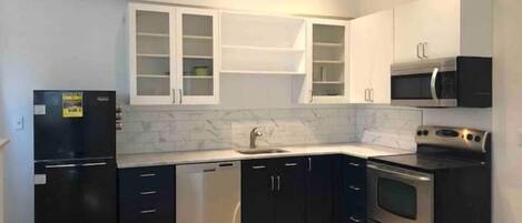 Una cocina moderna con armarios negros, un refrigerador de acero inoxidable, un microondas y un horno.