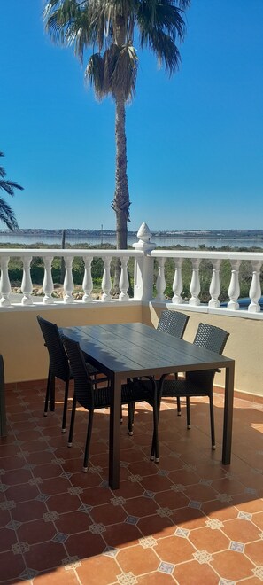 Una terraza con una mesa, sillas, una palmera y vistas al mar.