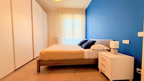 A bedroom with a bed, a nightstand, a dresser, a radiator, and a window with curtains. - Appartamento Dante  (Prato)