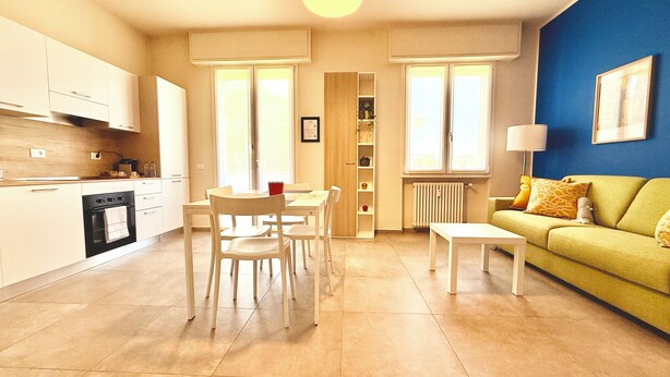 A modern kitchen with white cabinets and a dining area with a table and chairs. - Appartamento Dante  (Prato)