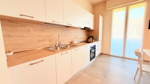 A modern kitchen with wooden cabinets, stainless steel appliances, and a sliding glass door leading to a balcony. - Appartamento Dante  (Prato)