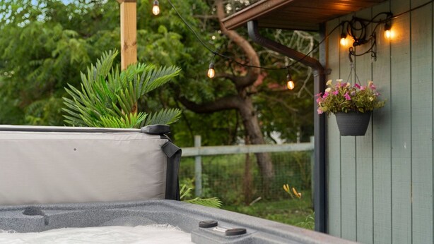 A hot tub with a stone base, surrounded by greenery and a hanging flower pot. - Near Ithaca!Hot Tub! LRG Home!Sleeps 12! Dogs ok! (Newfield)