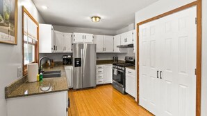 A modern kitchen with white cabinets, stainless steel appliances, and a wooden floor. - Near Ithaca!Hot Tub! LRG Home!Sleeps 12! Dogs ok! (Newfield)